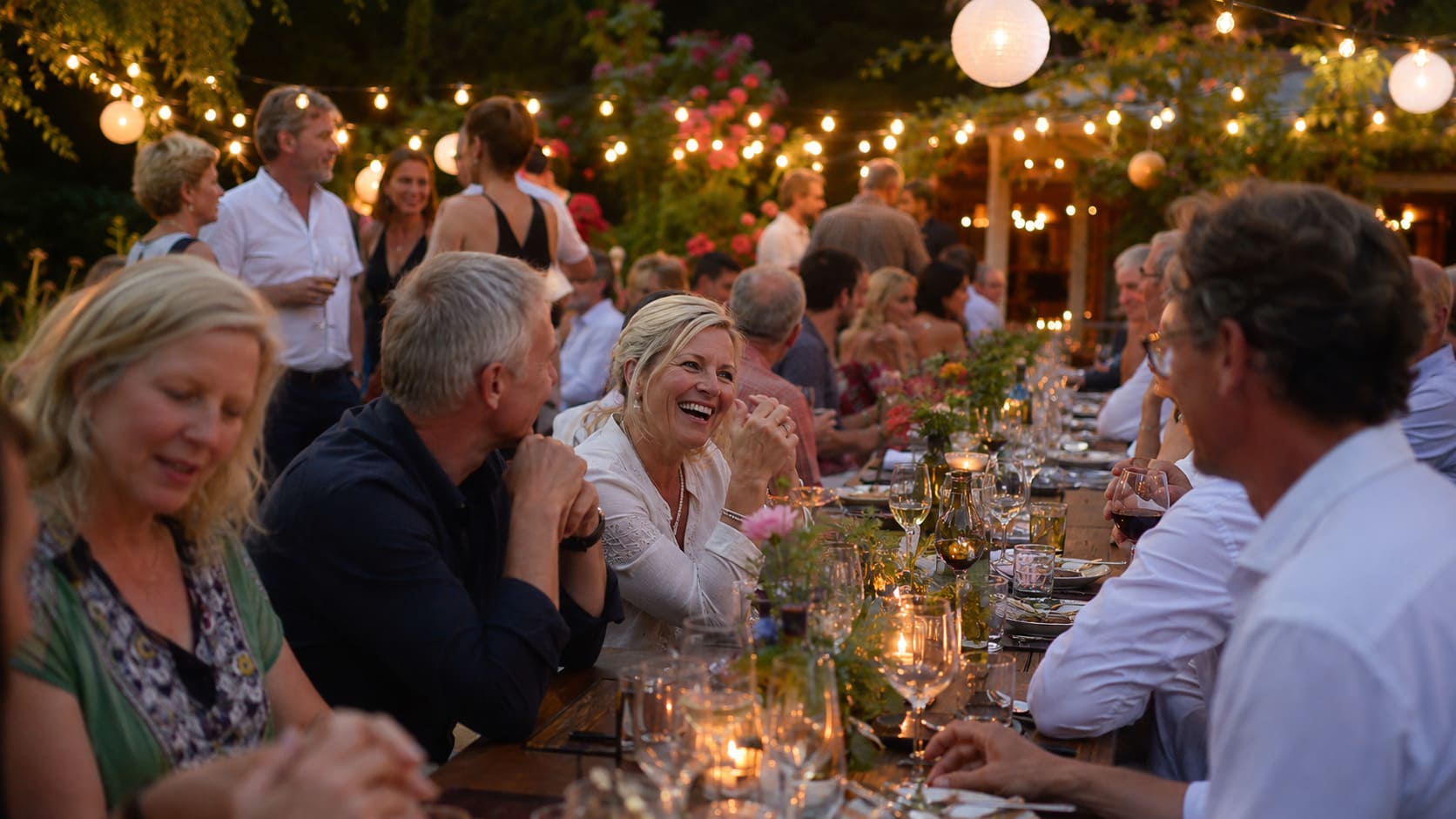 Stilvolle Gartenparty zum Geburtstag an einem Sommerabend mit langen Tischen und Lichterketten
